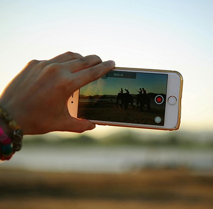 Mano sosteniendo un celular mientras graba videos en un destino turístico, representando el impacto del video marketing en el alcance y la conexión con la audiencia.